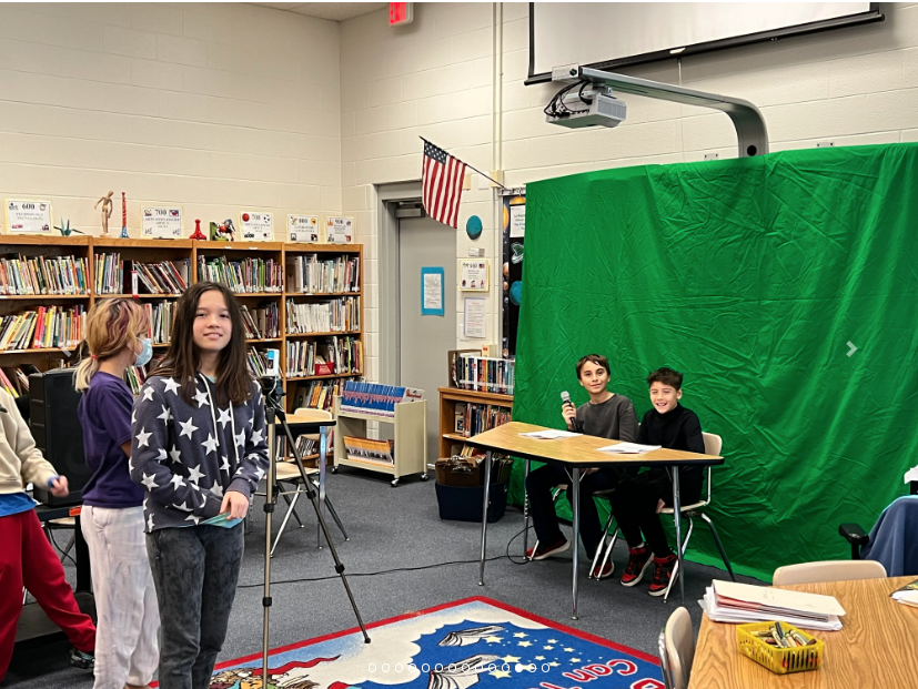 2 students in front of a green screen and one behind a camera on a tripod