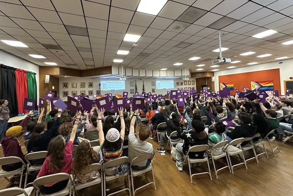 An auditorium filled with students holding up purple folders