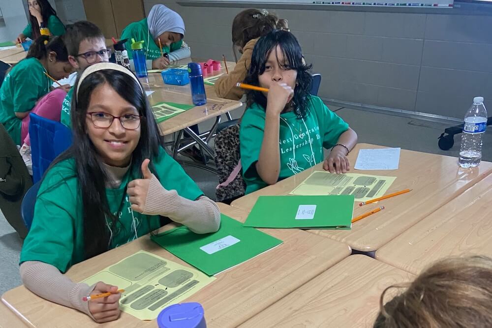 Two elementary school students smile as they work on a leadership activity together