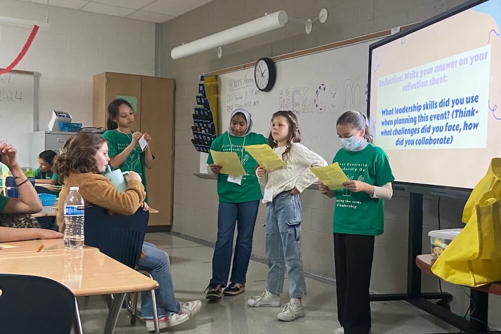 Three students stand up and present to a group of their peers
