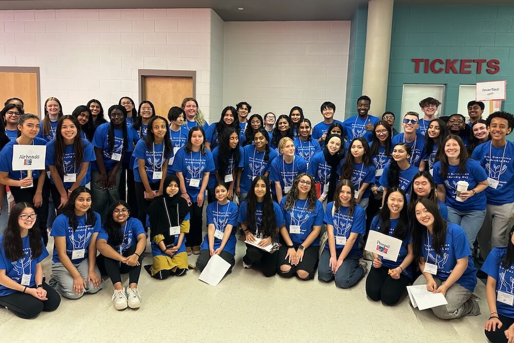 A large group of workshop presenters and volunteers in blue shirts stand in a semi-circle